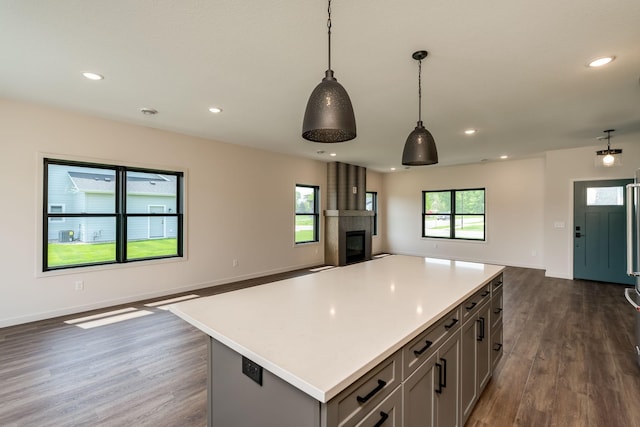 kitchen with dark wood-type flooring, hanging light fixtures, gray cabinets, a fireplace, and a kitchen island