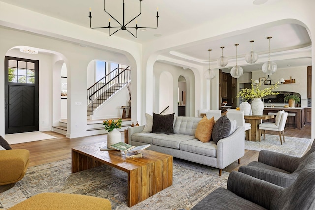 living room featuring a notable chandelier, a raised ceiling, light wood-type flooring, and sink