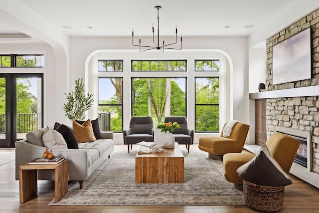 sitting room featuring a chandelier, wood-type flooring, a stone fireplace, and plenty of natural light