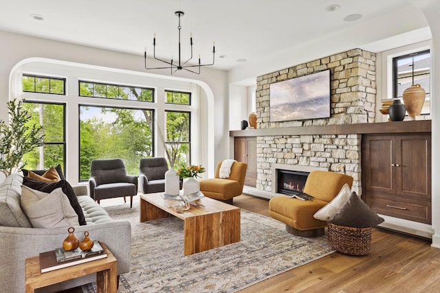 living room featuring a stone fireplace, wood-type flooring, and a chandelier