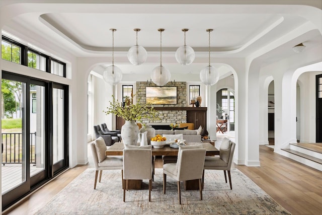 dining room featuring a fireplace, light wood-type flooring, and a raised ceiling