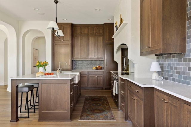 kitchen with pendant lighting, backsplash, a center island with sink, sink, and stainless steel electric range oven