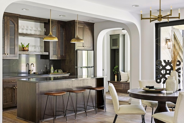 bar featuring dark wood-type flooring, sink, tasteful backsplash, decorative light fixtures, and stainless steel refrigerator