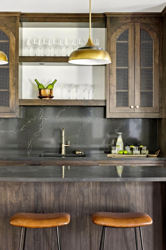 bar featuring tasteful backsplash, dark brown cabinetry, sink, and decorative light fixtures