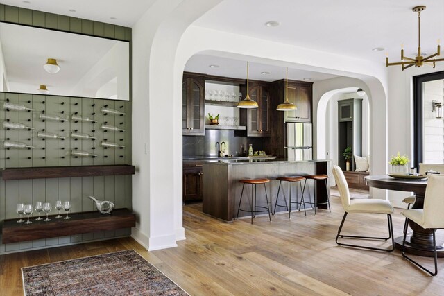 bar with pendant lighting, stainless steel fridge, dark brown cabinetry, and light wood-type flooring