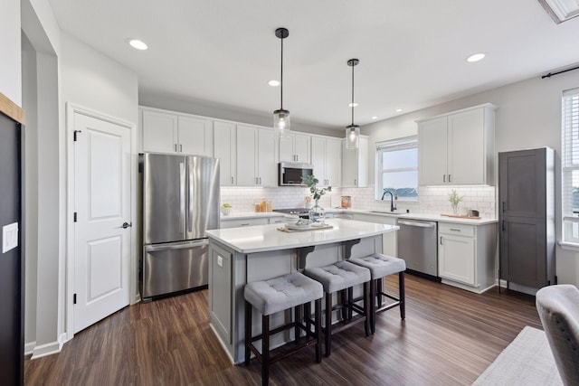 kitchen featuring stainless steel appliances, sink, decorative light fixtures, white cabinets, and a kitchen island