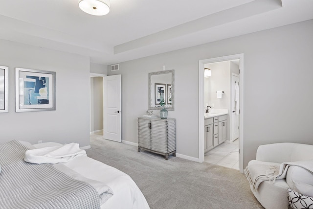 carpeted bedroom with a raised ceiling and connected bathroom