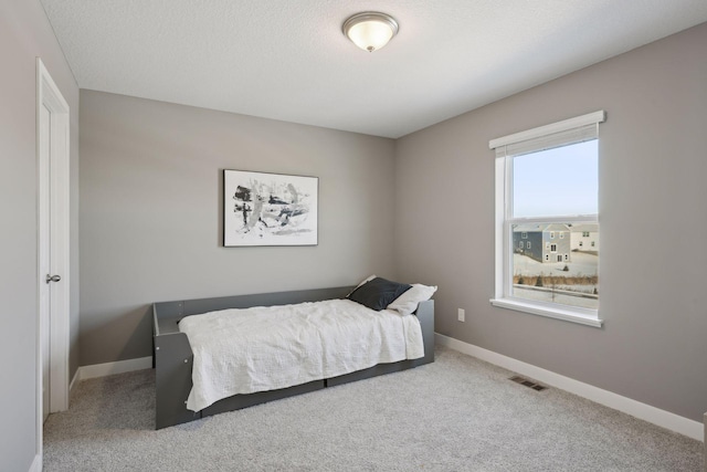 carpeted bedroom featuring a textured ceiling, visible vents, and baseboards