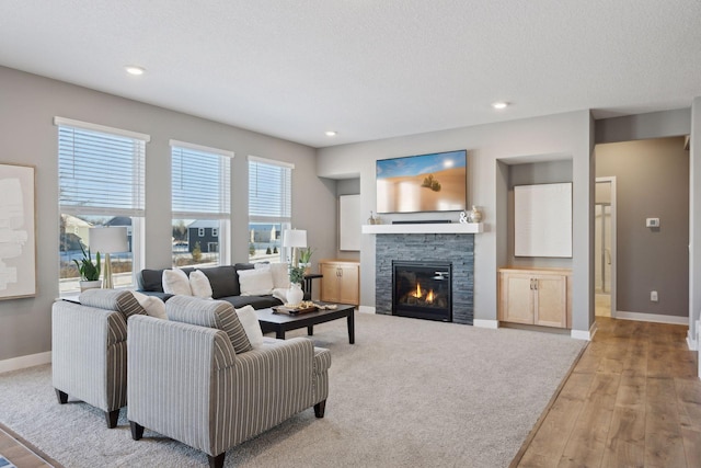 living area with a textured ceiling, light wood-type flooring, a fireplace, and baseboards