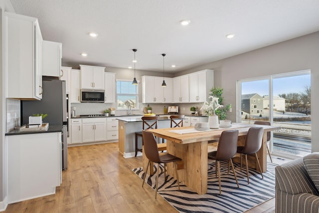 kitchen with stainless steel microwave, dark countertops, decorative light fixtures, and white cabinetry