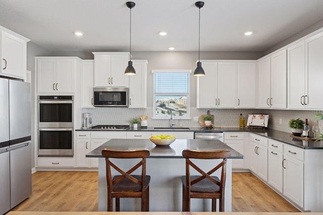 kitchen featuring pendant lighting, dark countertops, appliances with stainless steel finishes, white cabinets, and a sink