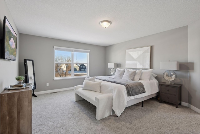 bedroom featuring light carpet, a textured ceiling, visible vents, and baseboards