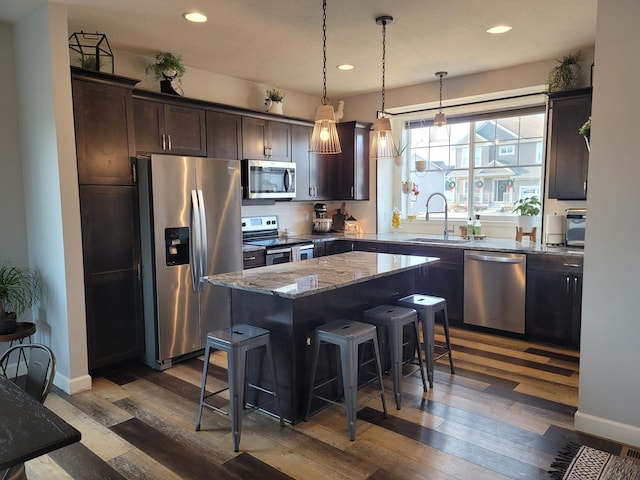 kitchen with stainless steel appliances, dark wood-type flooring, light stone counters, a kitchen island, and dark brown cabinetry