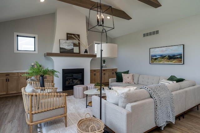 living room featuring a large fireplace, lofted ceiling with beams, a notable chandelier, and light hardwood / wood-style floors