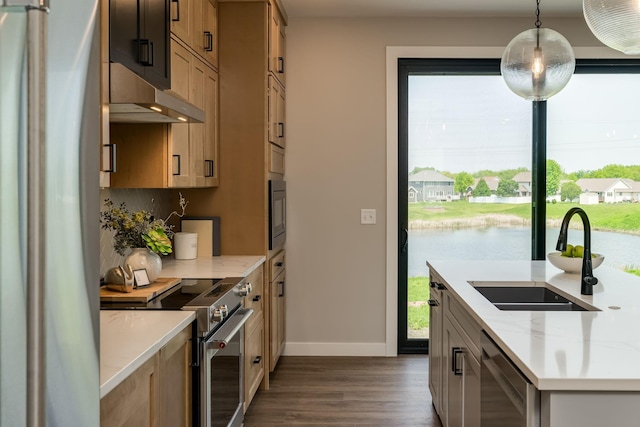 kitchen with a water view, sink, appliances with stainless steel finishes, decorative light fixtures, and light stone counters