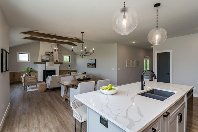 kitchen featuring light stone countertops, sink, decorative light fixtures, vaulted ceiling with beams, and an island with sink