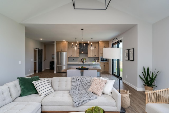 living room featuring high vaulted ceiling, an inviting chandelier, sink, hardwood / wood-style flooring, and a barn door