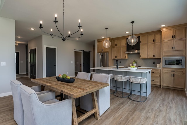 kitchen with a barn door, decorative backsplash, pendant lighting, a kitchen island with sink, and appliances with stainless steel finishes