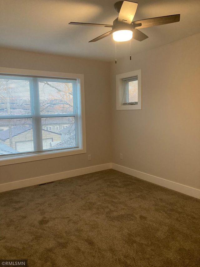 spare room featuring dark colored carpet, plenty of natural light, and ceiling fan