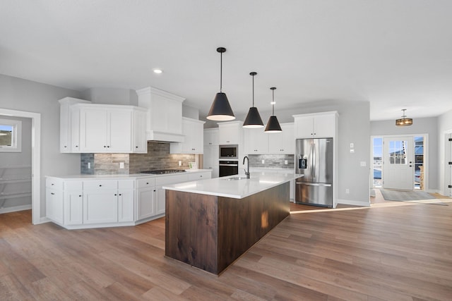 kitchen with tasteful backsplash, hanging light fixtures, white cabinets, stainless steel appliances, and a center island with sink