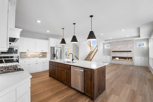 kitchen featuring pendant lighting, sink, a stone fireplace, an island with sink, and stainless steel appliances