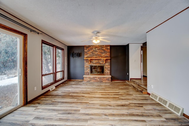 unfurnished living room with a brick fireplace, a textured ceiling, ceiling fan, and light hardwood / wood-style flooring