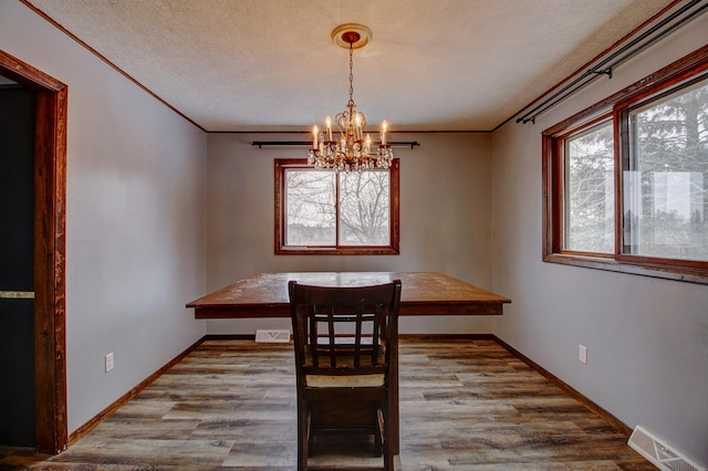 unfurnished dining area featuring a textured ceiling, light wood-type flooring, crown molding, and a notable chandelier