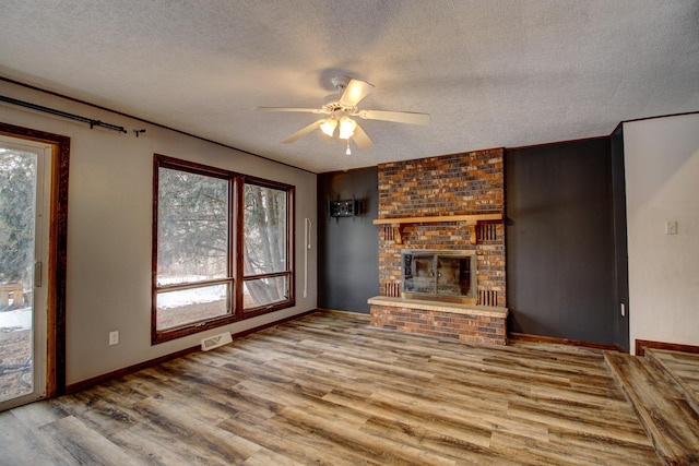 unfurnished living room featuring ceiling fan, a brick fireplace, hardwood / wood-style floors, and a textured ceiling