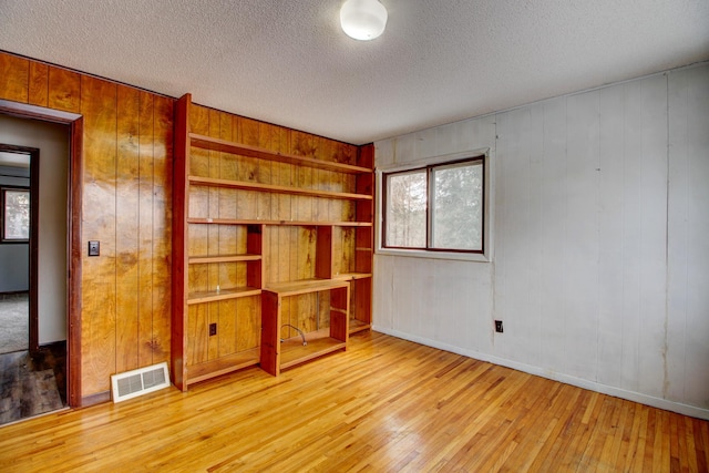 empty room with a textured ceiling, wooden walls, and wood-type flooring