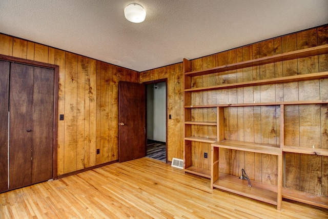 unfurnished bedroom featuring wood-type flooring, wooden walls, and a textured ceiling