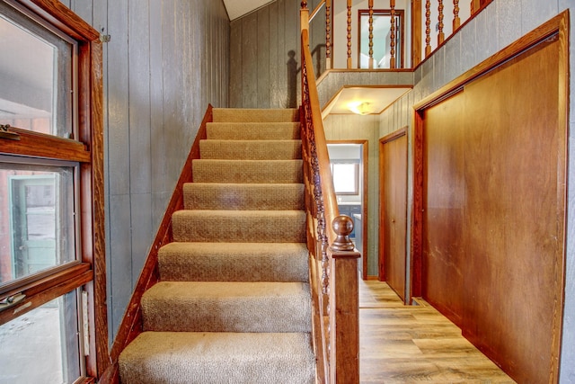 stairs with wooden walls, a wealth of natural light, and hardwood / wood-style flooring