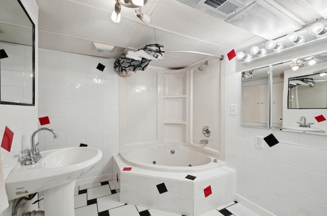 bathroom featuring a textured ceiling, tiled shower / bath combo, sink, and tile walls