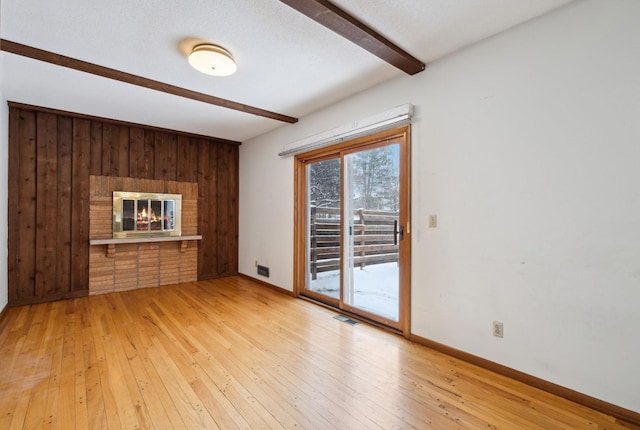 unfurnished living room with beamed ceiling, light hardwood / wood-style floors, a fireplace, and wooden walls