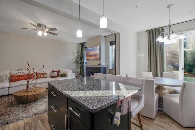 kitchen featuring light stone countertops, ceiling fan with notable chandelier, light hardwood / wood-style flooring, and hanging light fixtures