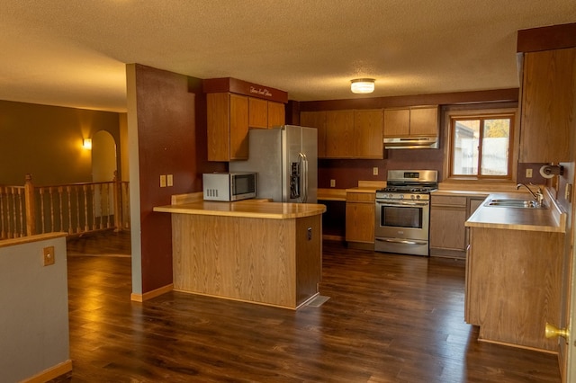 kitchen featuring sink, dark wood-type flooring, stainless steel appliances, a textured ceiling, and kitchen peninsula