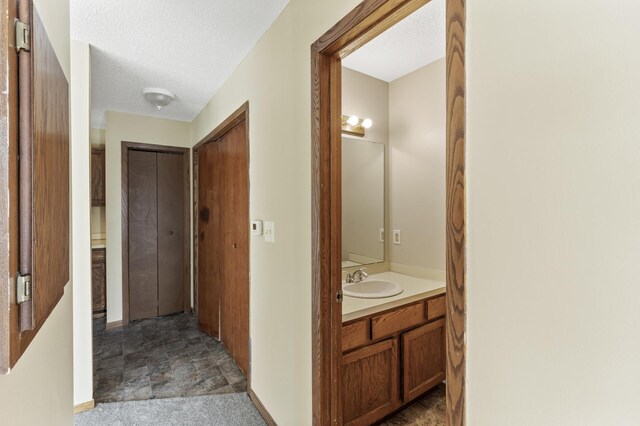 corridor with carpet flooring, sink, and a textured ceiling