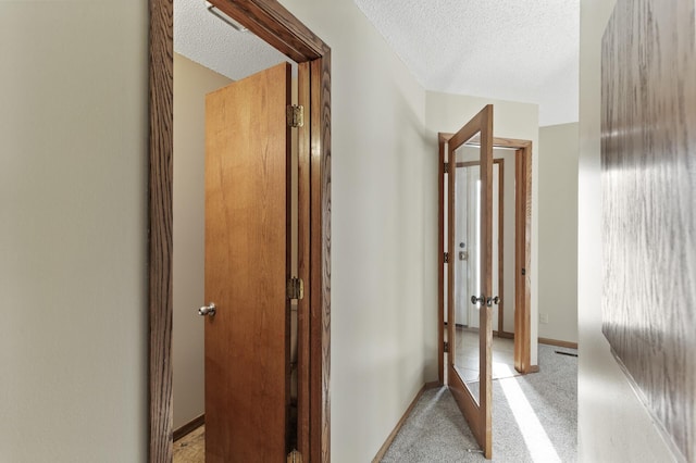 hall featuring light colored carpet and a textured ceiling