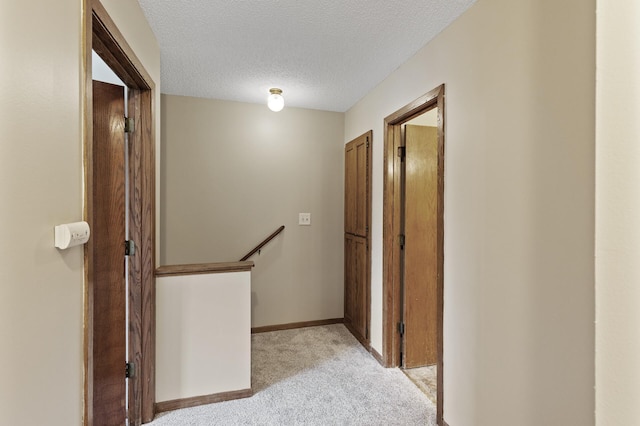 corridor with light colored carpet and a textured ceiling