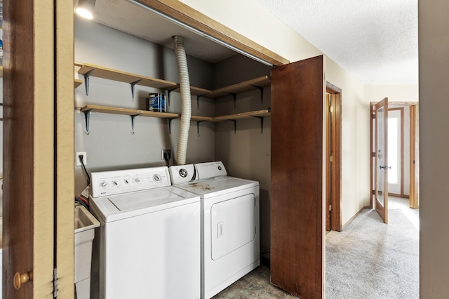 clothes washing area featuring washing machine and clothes dryer, light carpet, and a textured ceiling