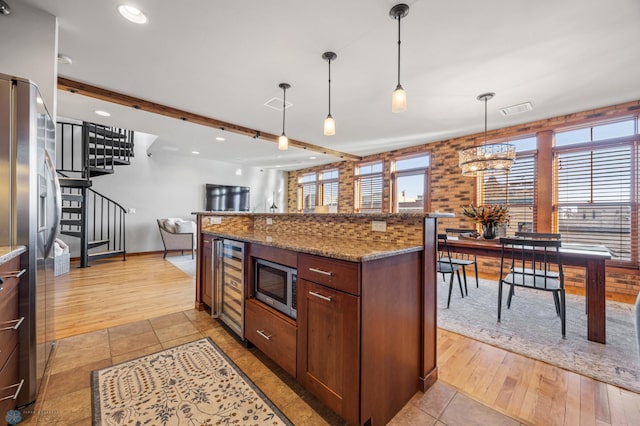 kitchen with dark stone counters, stainless steel appliances, beverage cooler, decorative light fixtures, and beamed ceiling