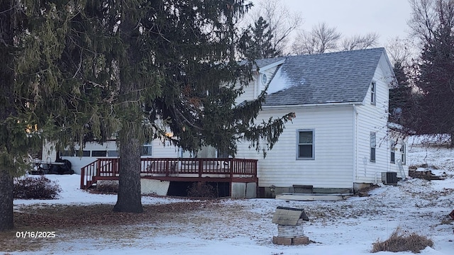 snow covered back of property with a deck and cooling unit