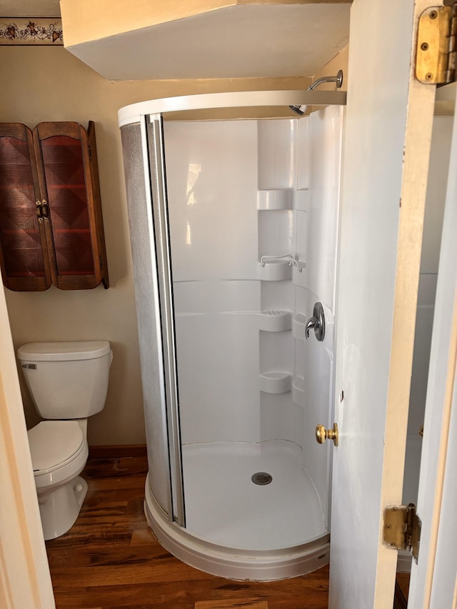 bathroom with hardwood / wood-style flooring, toilet, and a shower with door