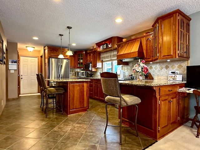 kitchen featuring a breakfast bar, custom range hood, decorative light fixtures, a center island, and stainless steel refrigerator