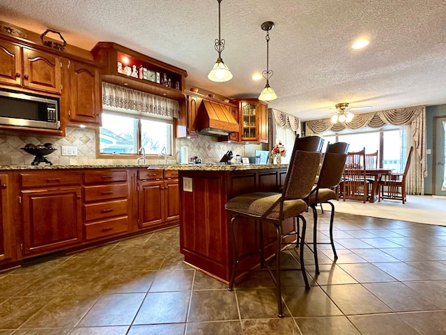 1606 Shore Dr, Worthington, MN 56187 - kitchen featuring stainless steel microwave, custom range hood, a textured ceiling, a ceiling fan, and backsplash