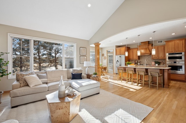 living room featuring light hardwood / wood-style flooring, sink, high vaulted ceiling, and decorative columns