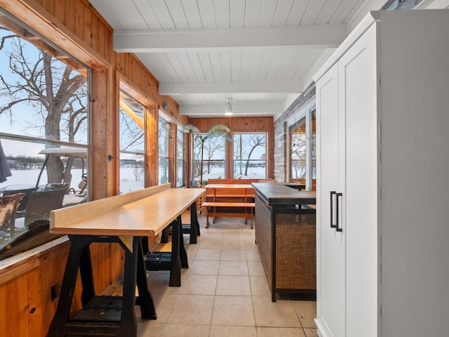 kitchen featuring beamed ceiling, light tile patterned floors, white cabinets, and wood walls