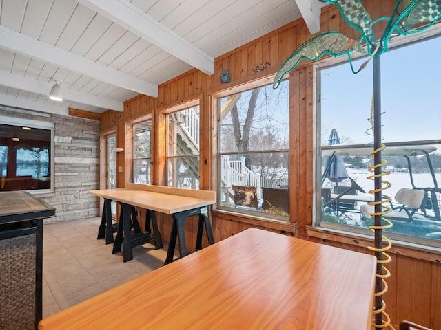 tiled dining room featuring beamed ceiling and wood walls