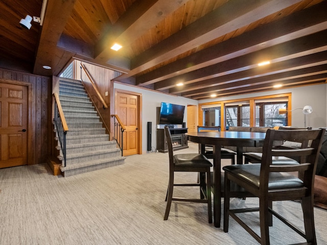 carpeted dining space featuring wooden ceiling, beam ceiling, and wood walls