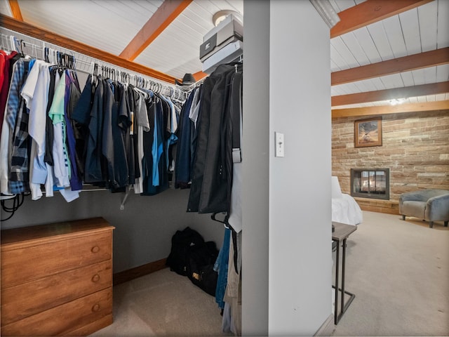 walk in closet featuring a stone fireplace, beamed ceiling, and carpet