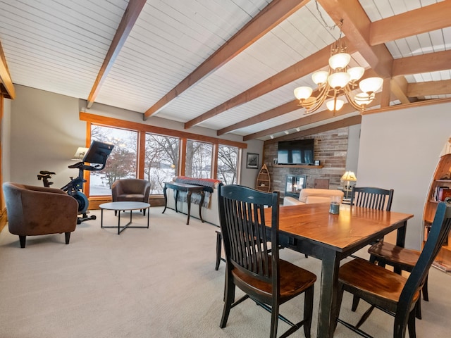 dining room with a notable chandelier, light colored carpet, a fireplace, and lofted ceiling with beams